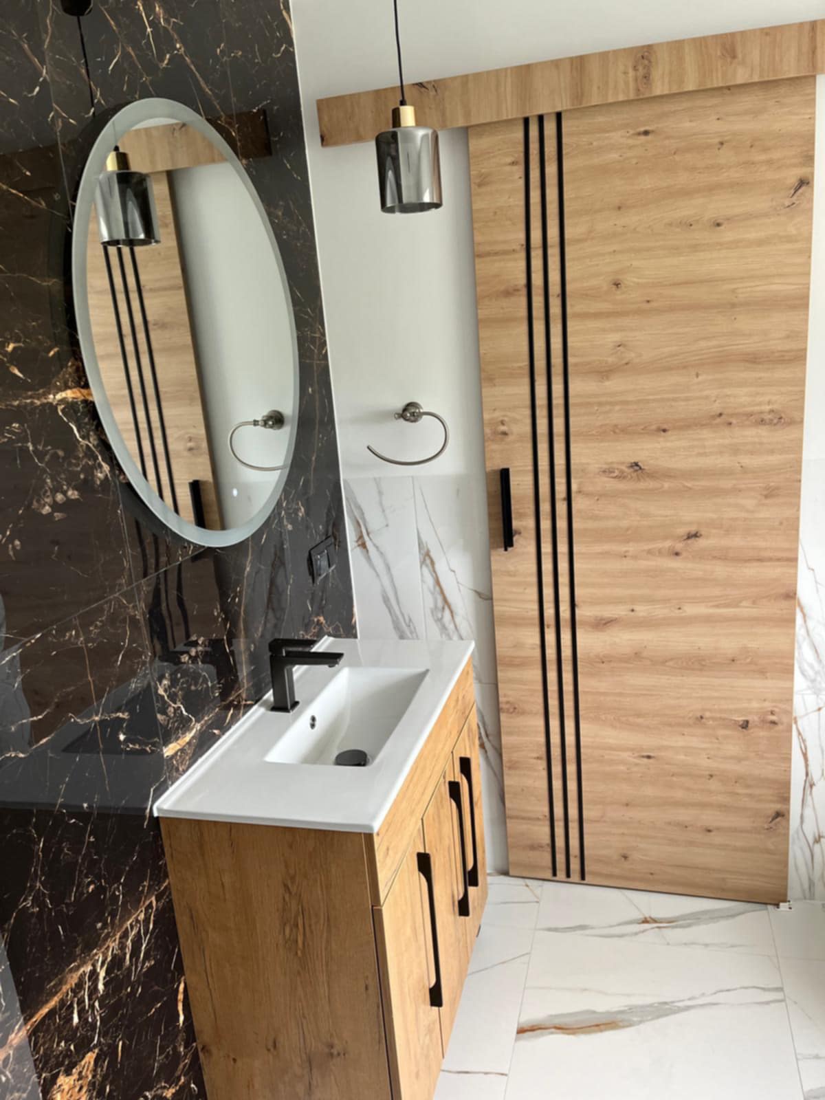 Nowoczesna łazienka z ciemnymi płytkami imitującymi marmur i szafką podumywalkową w kolorze drewna